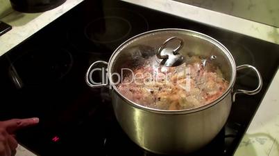 Control of the electric stove with a cooking shrimps in a saucepan.