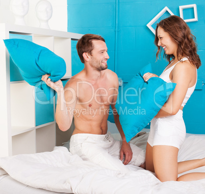 young couple having fun making pillows fight.