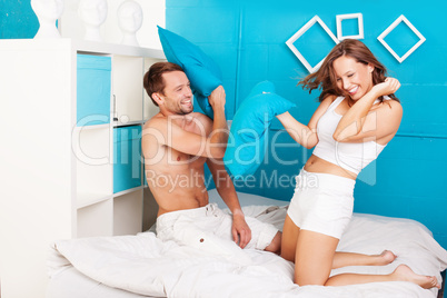 young couple having fun making pillows fight.