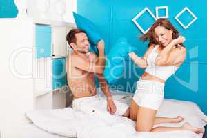 young couple having fun making pillows fight.