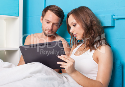 young couple browsing internet on tablet computer while sitting in bed