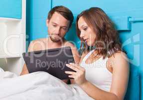 young couple browsing internet on tablet computer while sitting in bed
