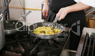 Chef cooking rigatoni with vegetables in a pan