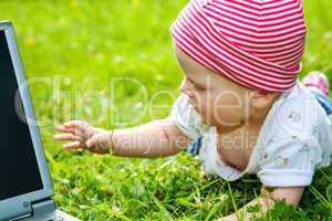 Small baby with laptop on the meadow
