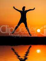 Silhouette woman jumping against orange sunset