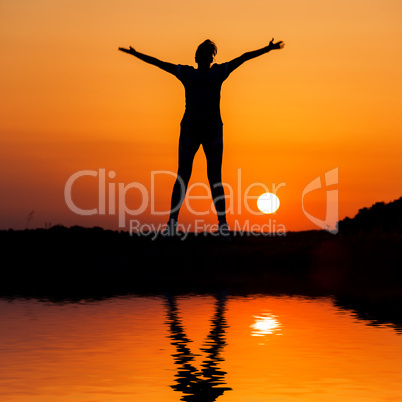 Silhouette woman jumping against orange sunset