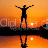 Silhouette woman jumping against orange sunset