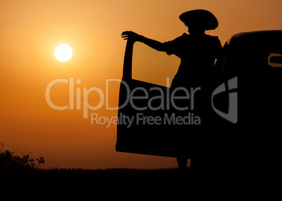 Silhouette woman with hat standing near car