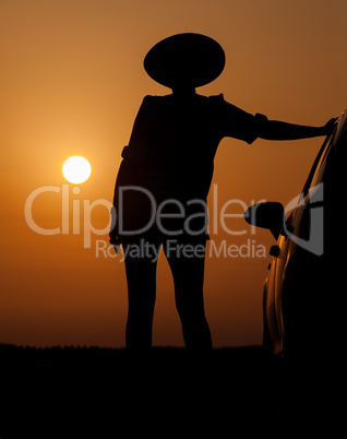 Silhouette woman with hat standing near car