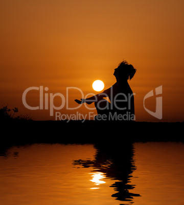 Silhouette woman sitting and relaxing against orange sunset