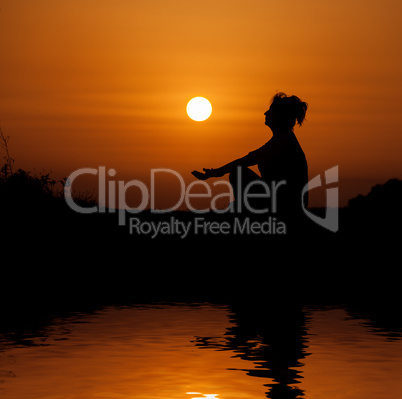 Silhouette woman sitting and relaxing against orange sunset