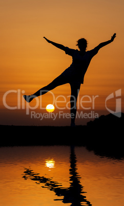 Silhouette woman jumping against orange sunset