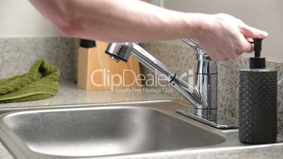 Man washes hands in kitchen sink and dries with green towel