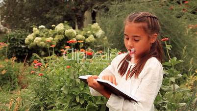 Young girl reading a book against flowers.