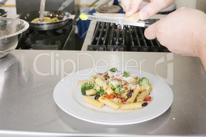 Italian food. Chef putting parmesan over a rigatoni with vegetab