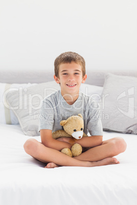 Little boy sitting on bed holding his teddy bear