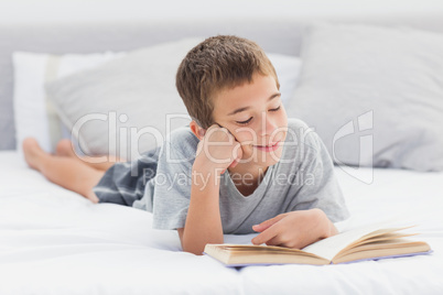 Little boy lying on bed reading book