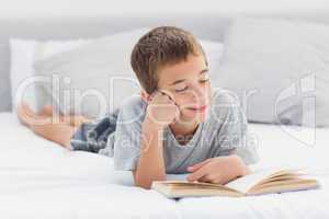 Little boy lying on bed reading book