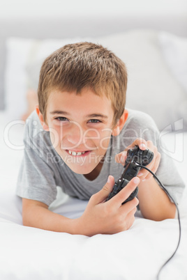 Concentrated little boy lying on bed playing video games