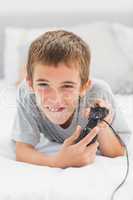 Concentrated little boy lying on bed playing video games