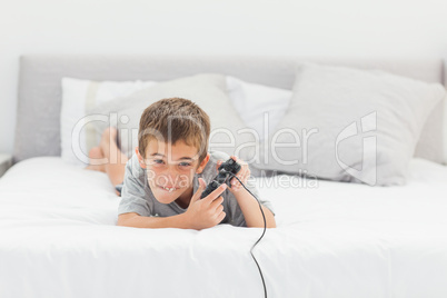 Little boy playing video games lying on bed