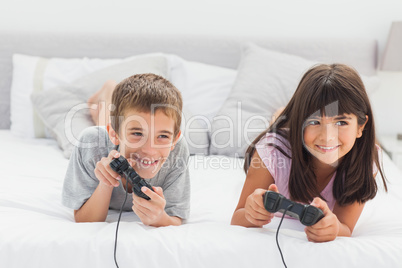 Siblings lying on bed playing video games