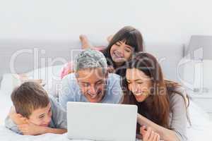 Family lying on bed using their laptop
