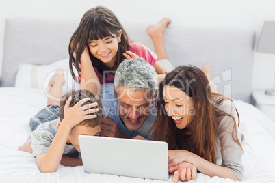 Smiling family lying on bed using their laptop