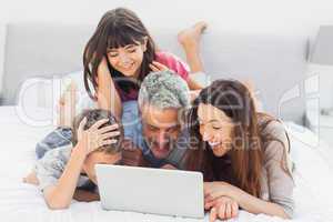 Smiling family lying on bed using their laptop