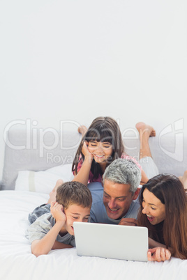 Happy family lying on bed using their laptop