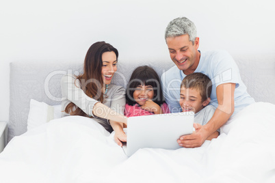 Family lying in bed using their laptop