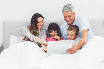 Smiling family lying in bed using their laptop