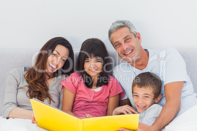 Smiling family looking together at their photograph album in bed