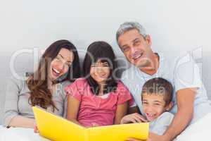 Smiling family looking together at their photograph album in bed