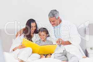 Parents with their son on bed looking together at photograph alb