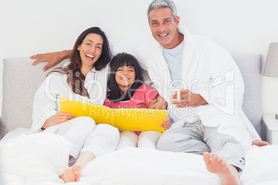 Parents with their daughter on bed looking together at photograp