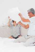 Father and son fighting together with pillows on bed