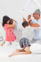 Father and his children fighting together with pillows on bed