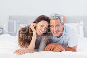 Couple lying on bed and smiling at camera