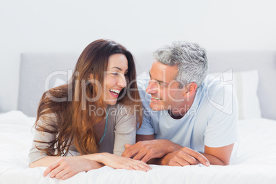 Happy couple lying on bed talking together