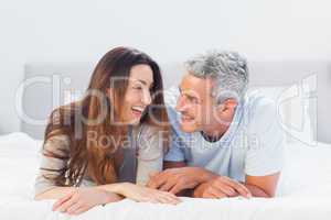 Happy couple lying on bed talking together