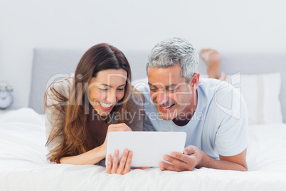 Couple lying on bed using their tablet pc