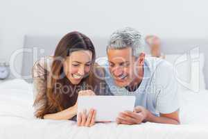 Couple lying on bed using their tablet pc
