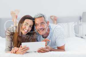 Cheerful couple lying on bed using their tablet pc