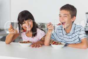 Smiling siblings eating cereal for breakfast in kitchen
