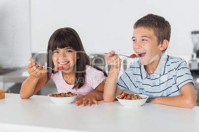 Happy siblings eating cereal for breakfast in kitchen