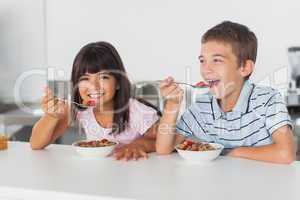 Happy siblings eating cereal for breakfast in kitchen