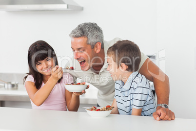 Little girl giving cereal to her father with brother smiling