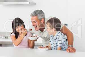 Little girl giving cereal to her father with brother smiling