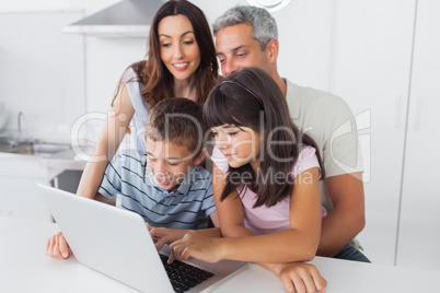 Family sitting in kitchen using their laptop